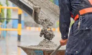 Robotnik w deszczu wylewa świeży beton do taczki. To właśnie jest beton – mieszanka cementu, kruszywa i wody.