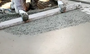 Ręce w rękawiczkach wyrównują świeży beton. Powstaje gładka powierzchnia, która wkrótce stanie się solidnym kubikiem betonu.