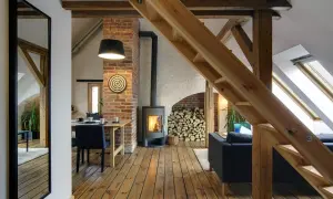 Przytulne poddasze użytkowe z kominkiem, drewnianymi belkami i schodami. Wygodny salon i jadalnia tworzą ciepłą atmosferę.