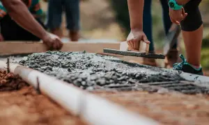 Ręce wygładzają świeży beton na fundamencie. Widać zbrojenie i rurę. Jaki beton na fundament? Ten wygląda na solidny.
