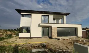 Nowoczesny dom w budowie z dużymi oknami i garażem, otoczony placem budowy.