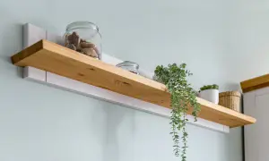 Drewniana półka z ukrytym mocowaniem, ozdobiona słoikami z przysmakami i zielonymi roślinami, tworzy przytulną aranżację.