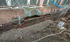 Widoczny pęknięty fundament z cegły, odsłonięty po wykopaniu ziemi. Widać ślady napraw i narzędzia.