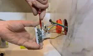Elektryk montuje gniazdko, podłączając 3 kable. Widać jego dłonie i narzędzia.