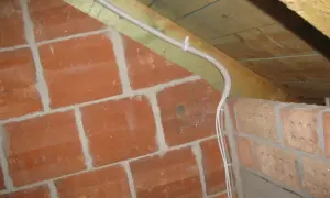 Instalacja elektryczna w peszlu na poddaszu, obok ceglanej ściany. Czy przewody elektryczne muszą być w peszlu? Tak, dla bezpieczeństwa.