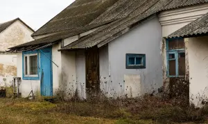 Stary budynek gospodarczy z niebieskimi drzwiami i oknami, porośnięty dziką roślinnością. Zastanawiasz się, jak zalegalizować budynek gospodarczy?