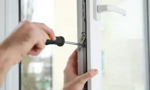 Regulacja docisku okna. Ręce majsterkowicza dokręcają śrubę w mechanizmie okna, aby zapewnić jego szczelność.