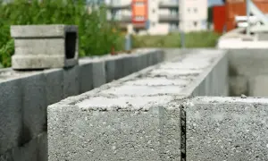 Budowa trwa. Zbrojenie pustaków szalunkowych na fundamencie. W tle budynki mieszkalne.
