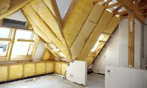 Strych w trakcie izolacji. Drewniana konstrukcja dachu i okna połaciowe otoczone żółtą wełną mineralną.