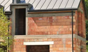 Budowa domu w toku. Widoczne ocieplenie nadproża pod rolety, czerwona cegła, dach i okna.
