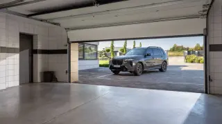 Nowa, nowoczesna brama garażowa strzela przy otwieraniu, odsłaniając luksusowego SUV-a na podjeździe.