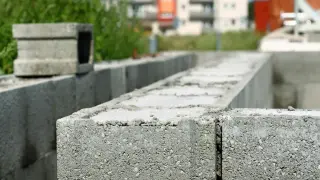Budowa trwa. Zbrojenie pustaków szalunkowych na fundamencie. W tle budynki mieszkalne.