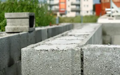 Budowa trwa. Zbrojenie pustaków szalunkowych na fundamencie. W tle budynki mieszkalne.