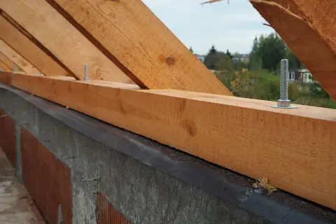 Zbrojenie wieńca pod murłatę: drewniane krokwie mocowane śrubami do betonowego wieńca, przygotowanie do budowy dachu.