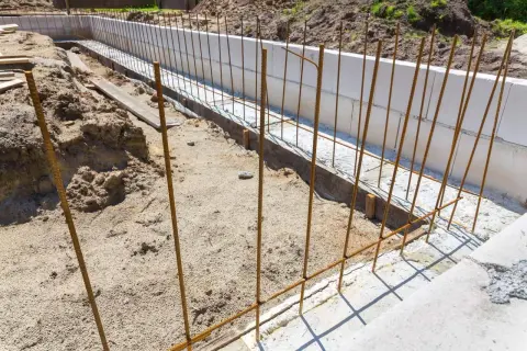 Zbrojenie z prętów stalowych B500SP w wykopie pod fundamenty. W tle białe bloczki betonowe.