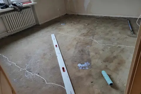 Wylewka w bloku z wielkiej płyty czeka na wykończenie. Położono białe linie, widać łaty i narzędzia: poziomicę i wałek.