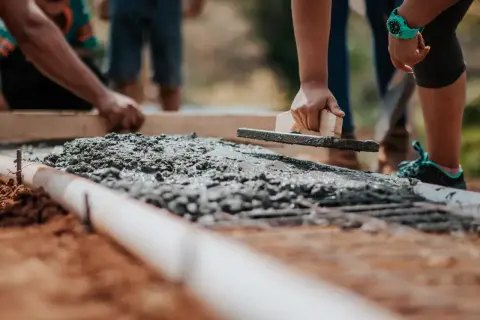 Ręce wygładzają świeży beton na fundamencie. Widać zbrojenie i rurę. Jaki beton na fundament? Ten wygląda na solidny.