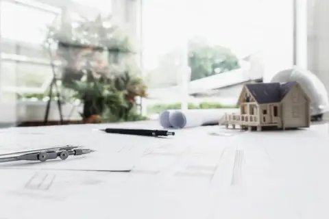 Model domu, plany, cyrkiel i ołówek na biurku. Architekt planuje drugą linię zabudowy.