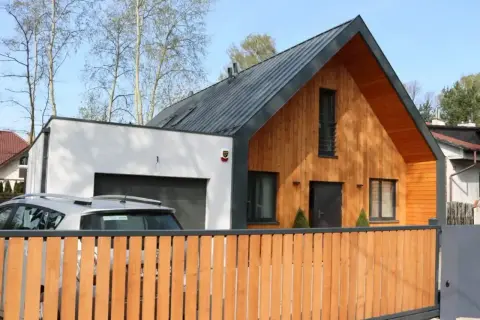 Nowoczesny dom z murowaną częścią i garażem, do którego przylega dobudówka drewniana.