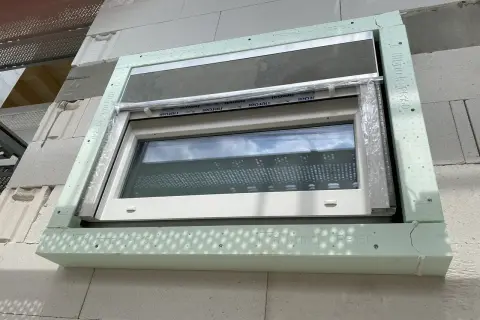 Nowe okno w trakcie ciepłego montażu, otoczone zielonym profilem izolacyjnym.