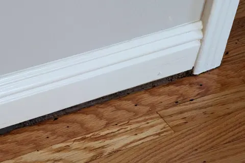 Widoczna szczelina między ościeżnicą a podłogą, wypełniona ciemnym materiałem, świadczy o potrzebie remontu.