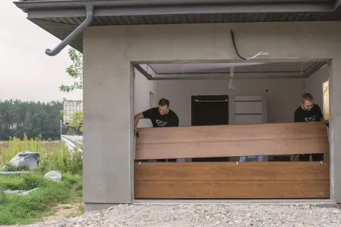 Dwóch mężczyzn montuje nowe panele, realizując wymianę okleiny na bramie garażowej.