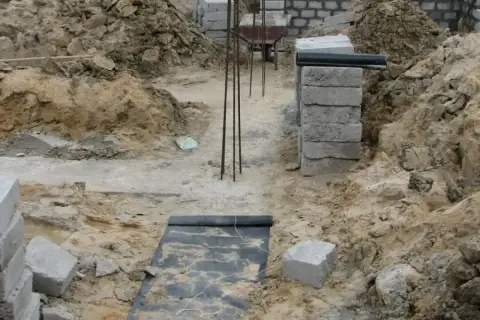 Budowa domu w toku. Widoczne wykopy, zbrojenie i materiały budowlane, tworzące fundamenty domu.