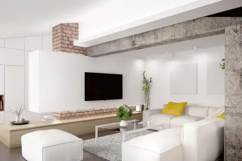 Nowoczesny salon z białym narożnikiem, telewizorem i ceglanym elementem architektonicznym, który pełni funkcję podciągu zamiast ściany nośnej.
