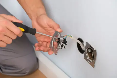 Ręce majsterkowicza przykręcają śrubokrętem mechanizm gniazdka. Trwa zerowanie gniazdka, przygotowanie do montażu.