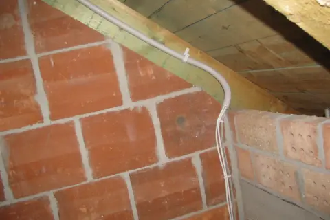 Instalacja elektryczna w peszlu na poddaszu, obok ceglanej ściany. Czy przewody elektryczne muszą być w peszlu? Tak, dla bezpieczeństwa.