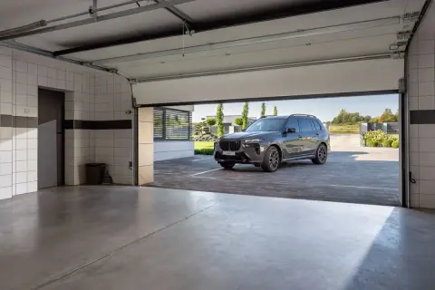 Nowa, nowoczesna brama garażowa strzela przy otwieraniu, odsłaniając luksusowego SUV-a na podjeździe.