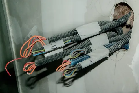 Przewody elektryczne w peszlach wychodzące ze ściany. Widać kolorowe żyły, gotowe do połączenia. To etap prac, jak przedłużyć przewód elektryczny w ścianie.