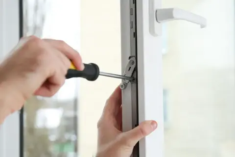 Regulacja docisku okna. Ręce majsterkowicza dokręcają śrubę w mechanizmie okna, aby zapewnić jego szczelność.