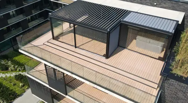 Nowoczesny taras na dachu z papy, z przeszklonym pawilonem i pergolą. Drewniana podłoga i szklane balustrady tworzą elegancką przestrzeń.