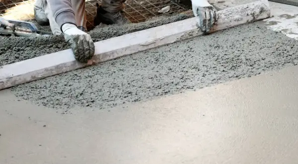 Ręce w rękawiczkach wyrównują świeży beton. Powstaje gładka powierzchnia, która wkrótce stanie się solidnym kubikiem betonu.