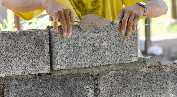 Murarz układa bloczki betonowe fundamentowe, tworząc solidną podstawę.