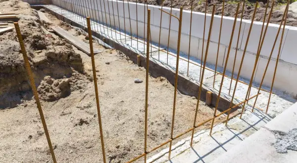 Zbrojenie z prętów stalowych B500SP w wykopie pod fundamenty. W tle białe bloczki betonowe.