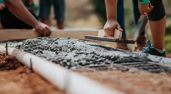 Ręce wygładzają świeży beton na fundamencie. Widać zbrojenie i rurę. Jaki beton na fundament? Ten wygląda na solidny.