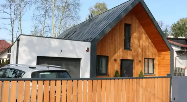 Nowoczesny dom z murowaną częścią i garażem, do którego przylega dobudówka drewniana.