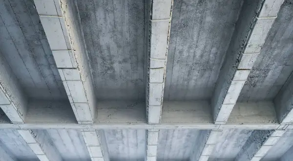 Widok od dołu na betonowy strop z belkami. Obliczenia obciążenia stropu żelbetowego na m2 są kluczowe dla bezpieczeństwa konstrukcji.