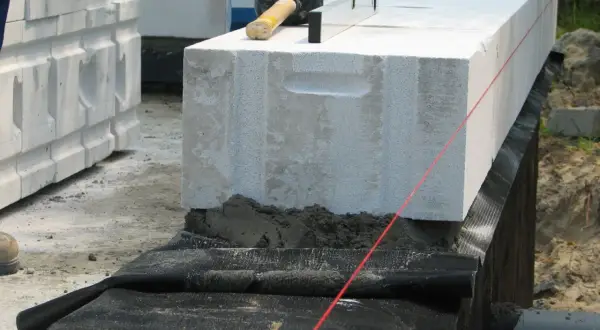 Budowa domu: układanie bloczków z betonu komórkowego, montaż izolacji poziomej fundamentów, poziomica i kielnia.