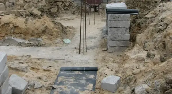 Budowa domu w toku. Widoczne wykopy, zbrojenie i materiały budowlane, tworzące fundamenty domu.