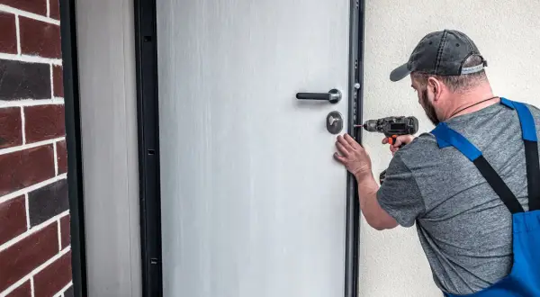 Fachowiec montuje nowe drzwi w bloku z wielkiej płyty. Wymiana drzwi poprawia bezpieczeństwo i estetykę.