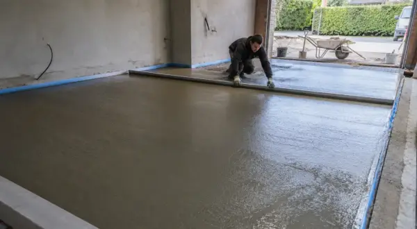 Pracownik wyrównuje świeżą wylewkę betonową, używając poziomicy. To kluczowy etap, jak zrobić prowadnice do wylewki, by uzyskać idealnie gładką powierzchnię.