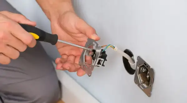 Ręce majsterkowicza przykręcają śrubokrętem mechanizm gniazdka. Trwa zerowanie gniazdka, przygotowanie do montażu.