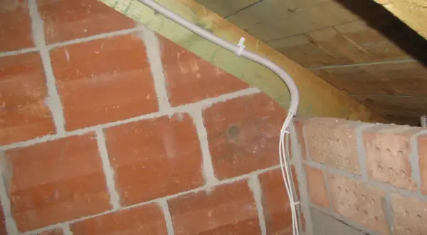 Instalacja elektryczna w peszlu na poddaszu, obok ceglanej ściany. Czy przewody elektryczne muszą być w peszlu? Tak, dla bezpieczeństwa.