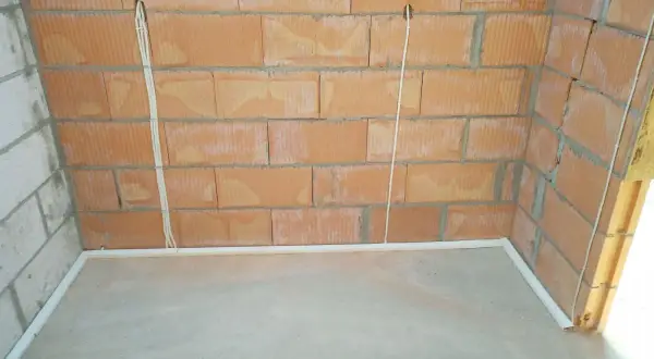 Widoczne przewody w posadzce bez peszla, biegnące od puszek instalacyjnych w ceglanej ścianie do podłogi.