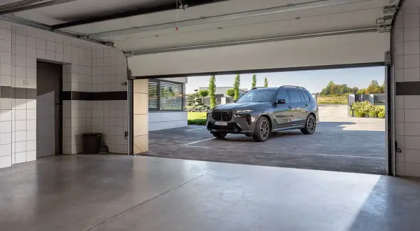 Nowa, nowoczesna brama garażowa strzela przy otwieraniu, odsłaniając luksusowego SUV-a na podjeździe.