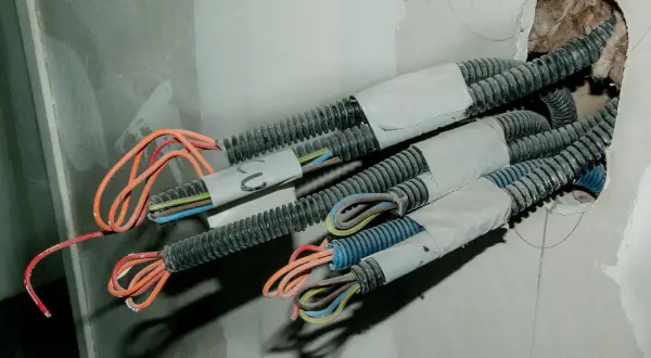 Przewody elektryczne w peszlach wychodzące ze ściany. Widać kolorowe żyły, gotowe do połączenia. To etap prac, jak przedłużyć przewód elektryczny w ścianie.