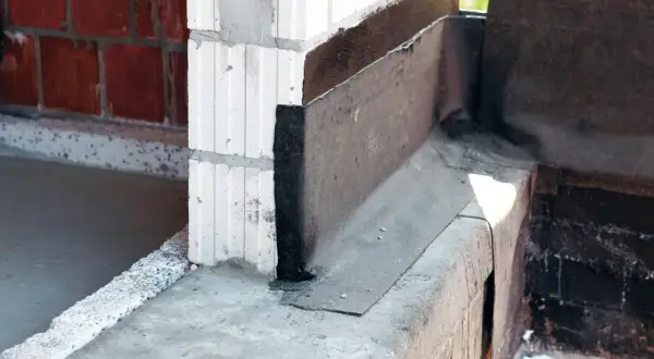Warstwa papy na fundamencie chroni przed wilgocią. Widoczny narożnik z izolacją.